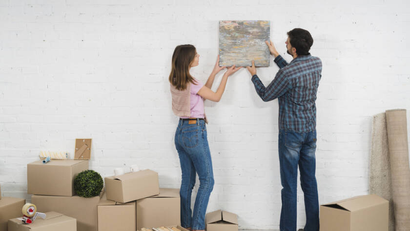 young-couple-placing-picture-frame-white-wall-with-cardboard-boxes