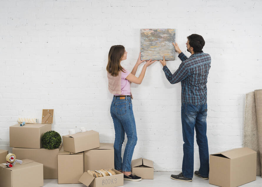 young-couple-placing-picture-frame-white-wall-with-cardboard-boxes